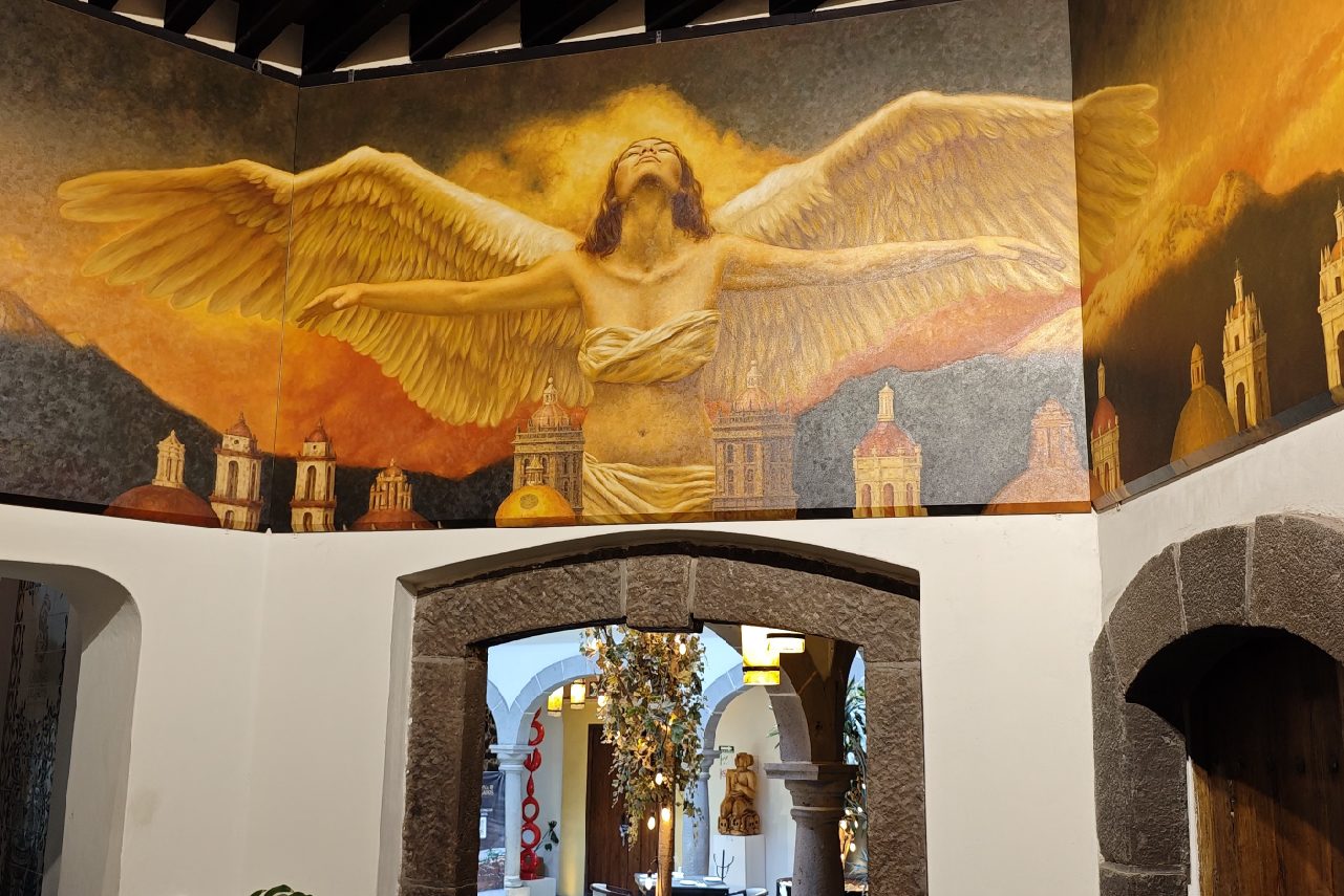 Mural “Ángel Custodio” de Fidel García en la Casona: un ángel con las alas abiertas sobre las cúpulas de Puebla.